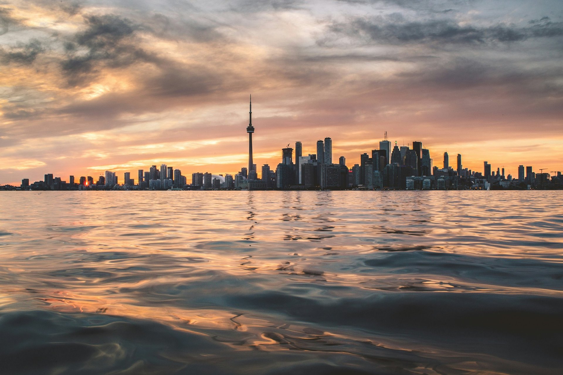 Toronto skyline at sunset with CN Tower and downtown buildings reflected in Lake Ontario water